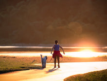 A woman walks her dog along a scenic path at sunset, capturing a peaceful moment.