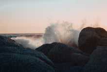A powerful ocean wave crashes against rocky coastline at sunset, capturing nature's force and beauty.