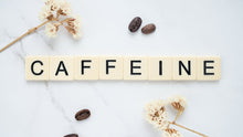 Scrabble tiles spelling caffeine with coffee beans on marble background.