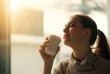 Smiling woman savoring morning coffee by the window in soft warm light.