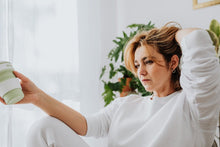 Thoughtful woman in casual attire holding a coffee cup in a cozy living room.
