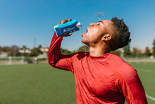 An athlete in a red shirt hydrates with maple water on a sunny day outdoors.