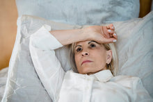 Contemplative woman in white shirt lying on bed, lost in thought. Indoor setting highlights tranquility.