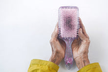 Close-up of senior hands holding a hairbrush with hair strands against a white backdrop.