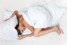 A serene image of a woman sleeping comfortably wrapped in a white duvet on a plain bed.