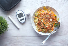 Top view of a nutritious vegetable salad next to diabetic monitoring equipment on a wooden table.