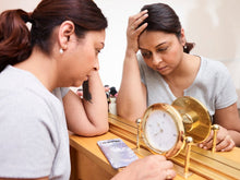 A woman looks pensive and tired, reflecting on burnout with a clock and mirror.
