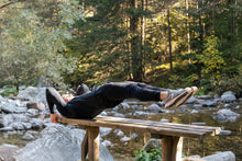 Man performing a core exercise on a bench by a serene river in a forest setting.