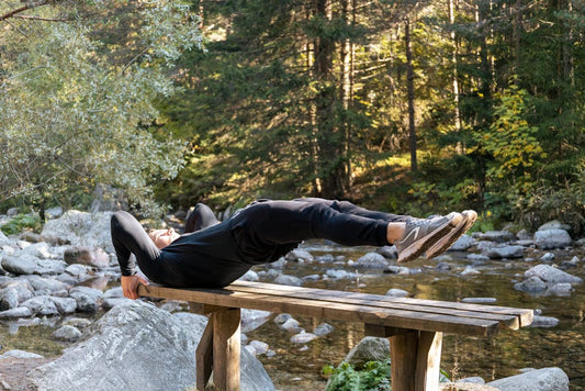 Man performing a core exercise on a bench by a serene river in a forest setting.