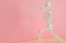 A skeleton model doing a yoga stretch on a pink backdrop, symbolizing fitness and anatomy.