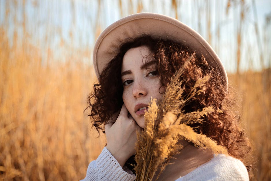 Artistic portrait of a woman outdoors with hat and dry reeds, warm tones