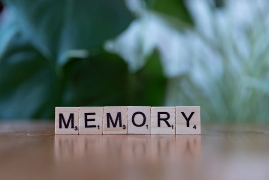 Wooden letter tiles spelling 'Memory' on a wooden table with blurred green background.