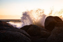 Sunlit ocean wave crashing against rocks creating a dramatic splash at sunset.