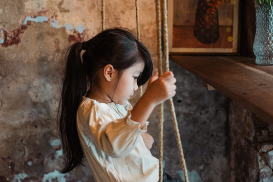 Thoughtful young girl sitting on a swing indoors, in a rustic setting with soft lighting.