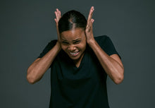 Portrait of an adult woman covering ears, looking irritated, against a dark background.