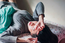 A woman resting on a bed indoors, expressing relaxation and tiredness.