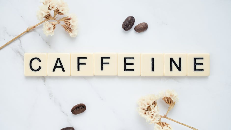Scrabble tiles spelling caffeine with coffee beans on marble background.