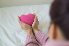 From above of unrecognizable female in sweater sitting on white blanket with pink heart shaped exercise ball in light room