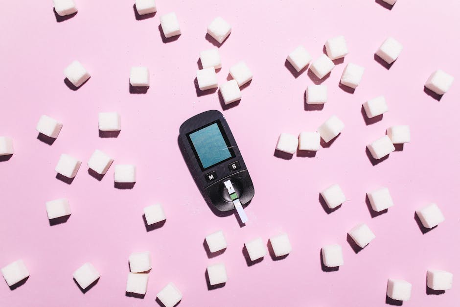 Blood glucose meter surrounded by sugar cubes on a pink background, highlighting diabetes awareness.