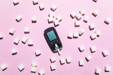 Blood glucose meter surrounded by sugar cubes on a pink background, highlighting diabetes awareness.