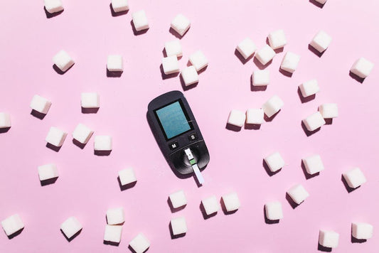 Blood glucose meter surrounded by sugar cubes on a pink background, highlighting diabetes awareness.