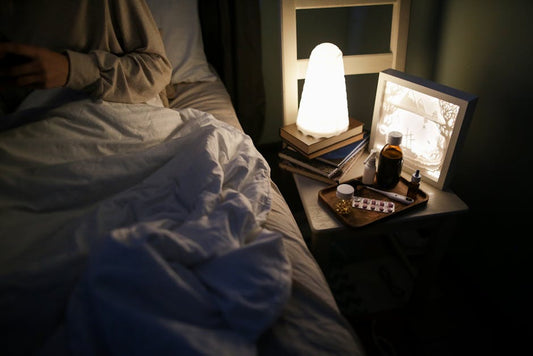 A bedside table with a lamp, books, and medicines for a cozy nighttime setting.