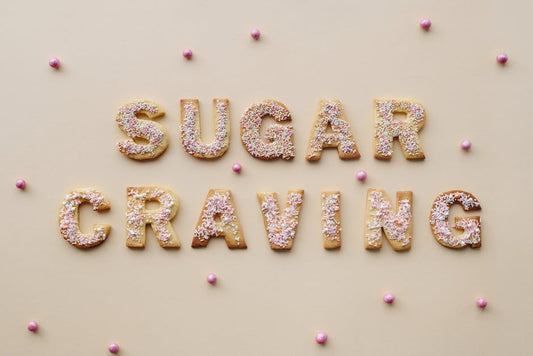 Flatlay of sprinkle-covered cookie letters spelling 'sugar craving' on a beige background.