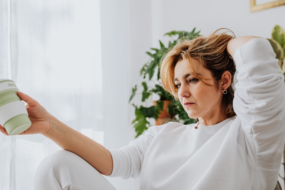 Thoughtful woman in casual attire holding a coffee cup in a cozy living room.