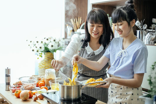 Happy mother and daughter cooking homemade long noodles in saucepan on electric hob in kitchen