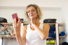 Middle-aged woman checking pulse on smartphone during fitness routine indoors.