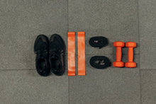 Flat lay of gym essentials including dumbbells, sneakers, and resistance bands on a grey floor.