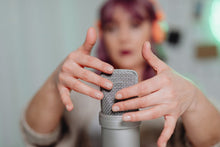 A woman gently touching a microphone during an ASMR recording session indoors.