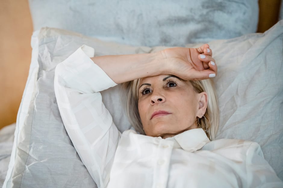 Contemplative woman in white shirt lying on bed, lost in thought. Indoor setting highlights tranquility.