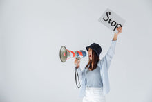 Woman passionately protesting with a megaphone and 'Stop' sign in a studio setting.