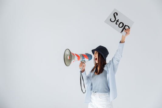 Woman passionately protesting with a megaphone and 'Stop' sign in a studio setting.