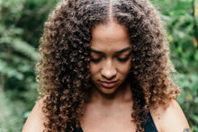 A serene woman with curly hair meditates peacefully in a lush outdoor setting.